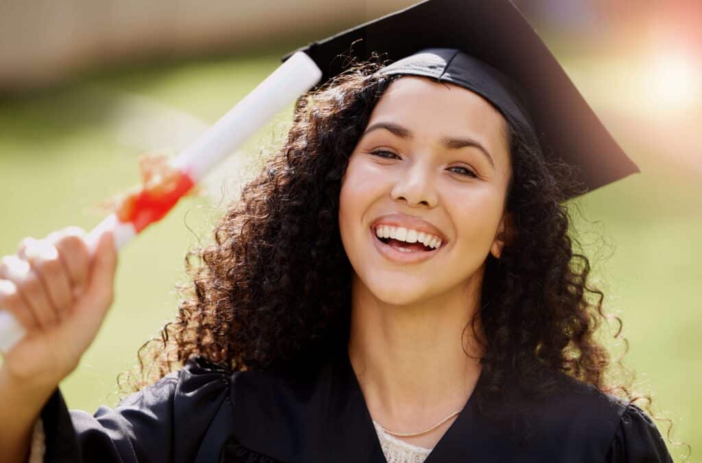 Young woman in cap and gown holding up her diploma